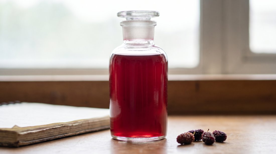 Organic mulberry juice sample in a glass apothecary bottle beside fresh mulberries, development stage
