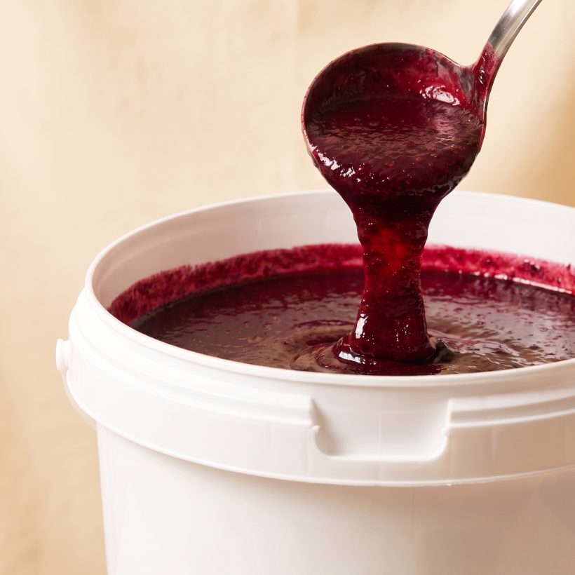 20 kg pail of raw organic mulberry puree, deep red-purple, ladle lifting the puree
